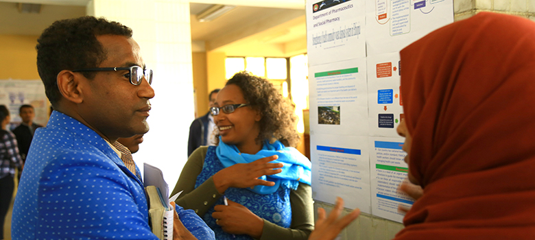 A man and woman stand in front of a poster conversing. 