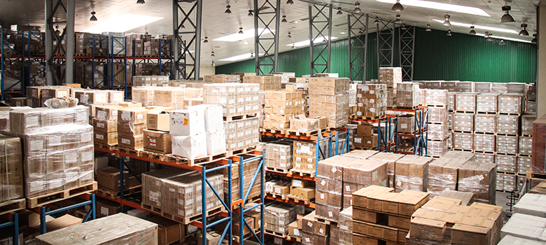 A large, brightly lit warehouse with cardboard boxes stacked high on pallets.
