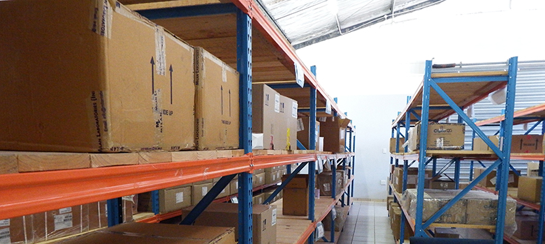 Rows of boxes of medicines sit on orange and blue shelves in pharmacy storage.