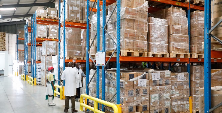 Image of a large central warehouse with proper storage of commodities and three properly masked employees.