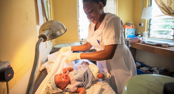 Image of Ghana midwife Veronica Finu smiling and tending to a newborn baby.