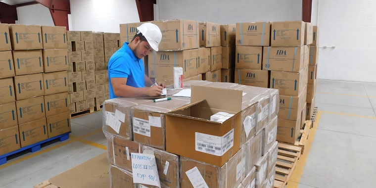 A man wearing a hard hat in a warehouse checking stock.