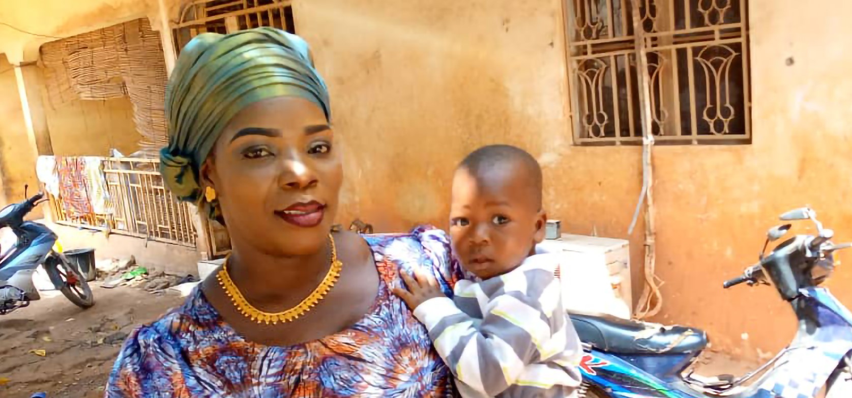 Malian mother and infants pose in sandy street in front of concrete home