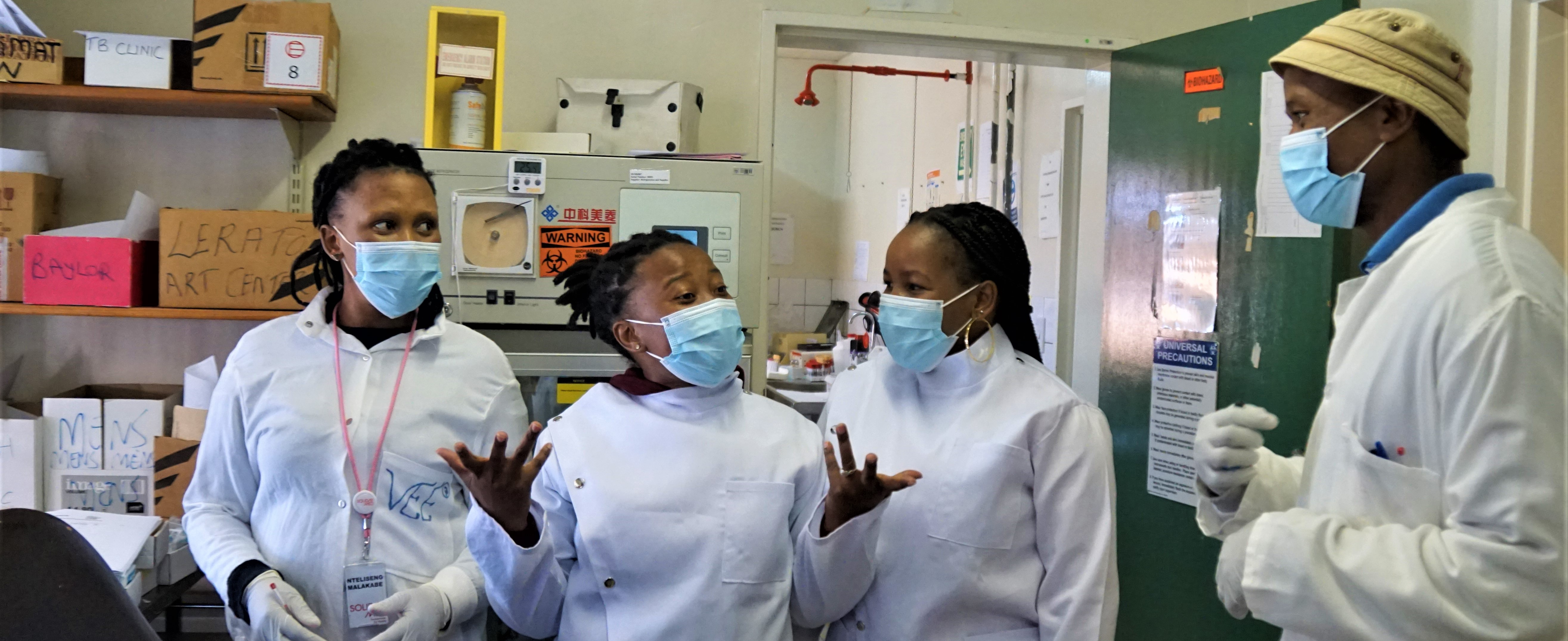 Masked lab techs in Lesotho discuss work in medical office