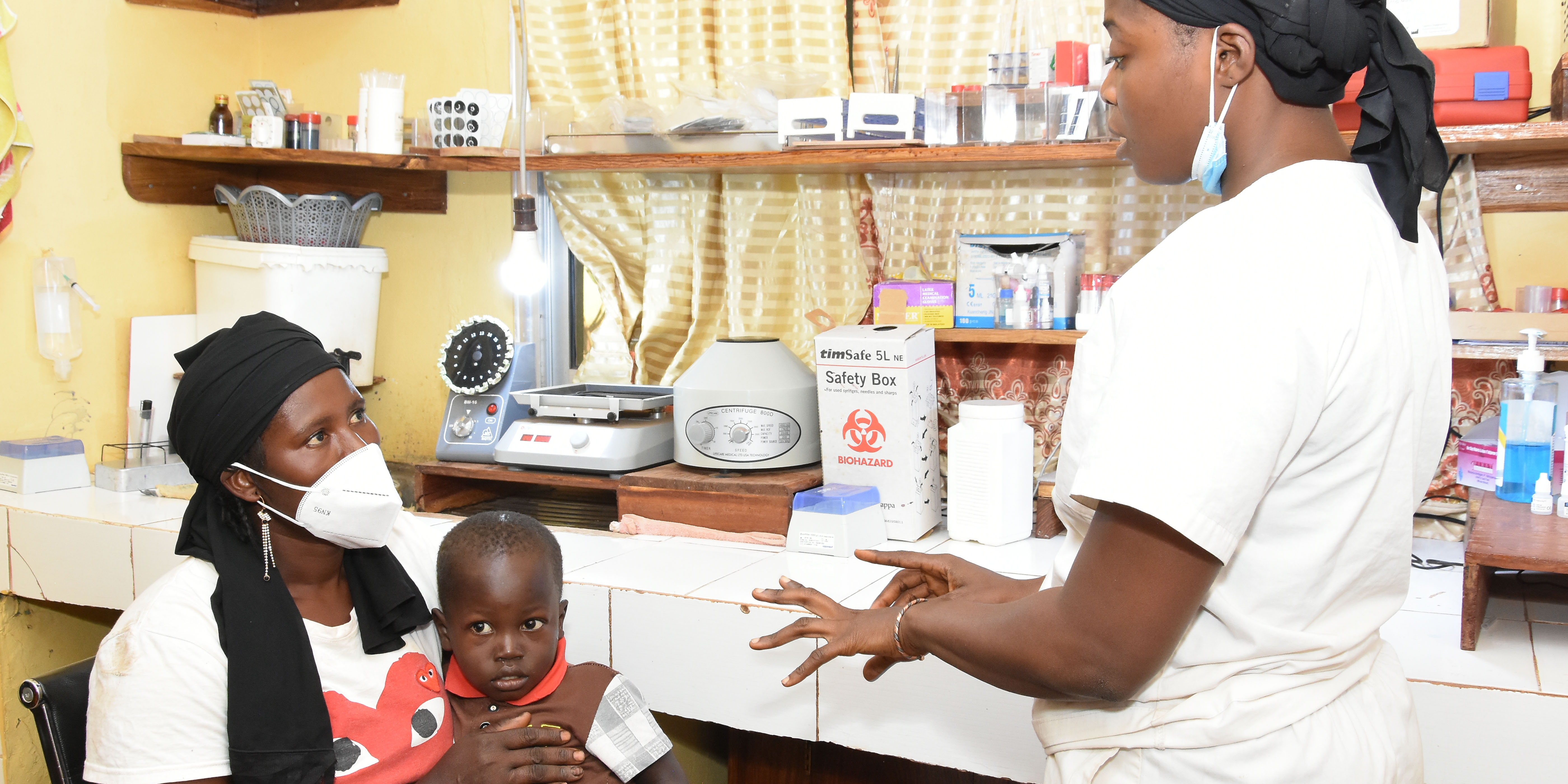 Guinean mother and child sit as health worker counsels in health facility room