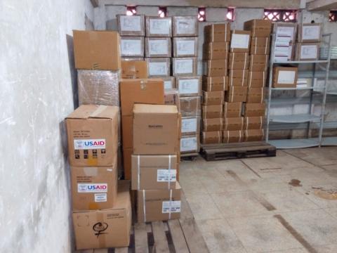 USAID-labeled boxes stacked in a store room.