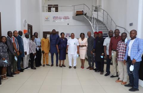 Nigerian government officials and contractors gather in semi circle facing camera in large, light-filled room.